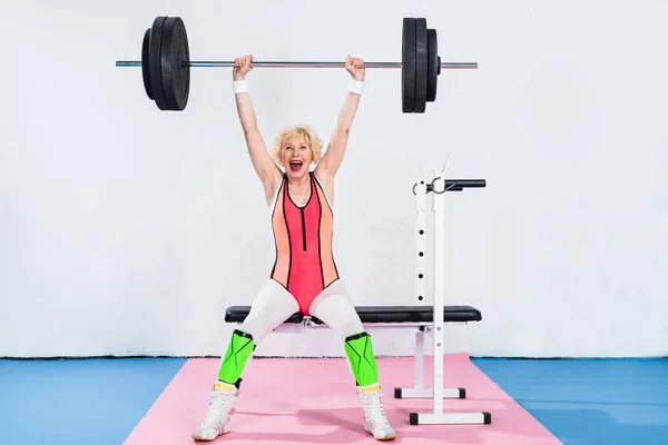 Excited senior sportswoman lifting barbell — Stock Photo