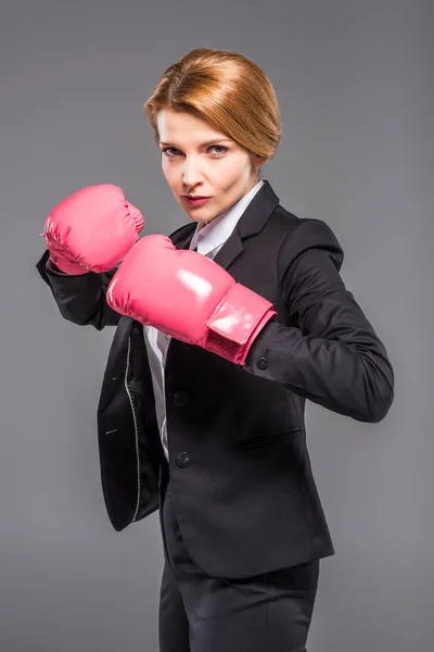 Hermosa empresaria confiada en traje y guantes de boxeo rosa, aislado en gris - foto de stock