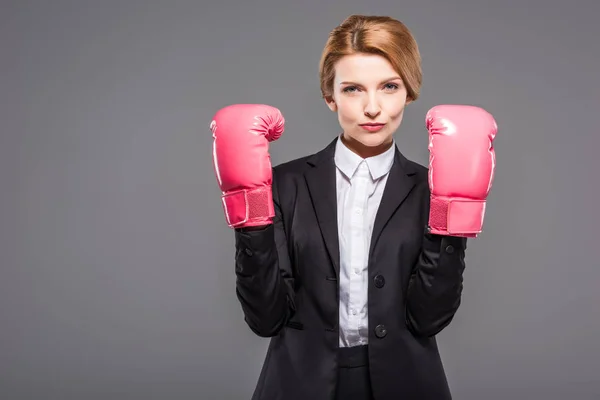 Seriöse Geschäftsfrau posiert in Anzug und rosa Boxhandschuhen, isoliert auf grau — Stockfoto