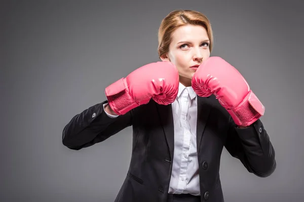 Attraente donna d'affari in abito e guanti da boxe rosa, isolato su grigio — Foto stock