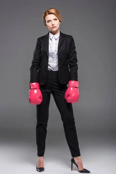 Mujer de negocios seria posando en traje y guantes de boxeo rosa, aislados en gris - foto de stock