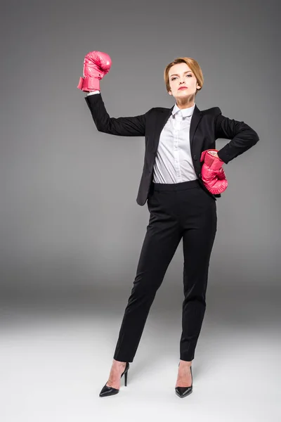 Fuerte mujer de negocios posando en ropa formal y guantes de boxeo, aislado en gris - foto de stock
