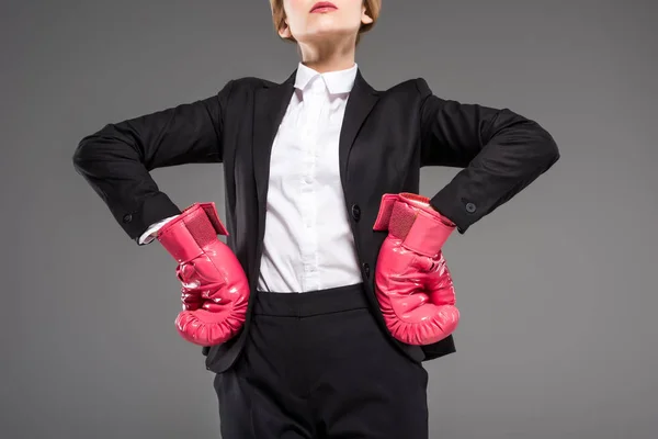 Vista recortada de la mujer de negocios fuerte posando en traje y guantes de boxeo rosa, aislado en gris - foto de stock