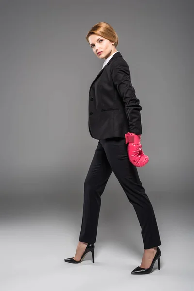 Femme d'affaires sérieuse en costume et gants de boxe rose, isolé sur gris — Photo de stock