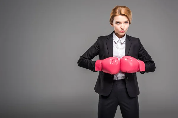 Mulher de negócios em terno e desgaste formal e luvas de boxe rosa, isolado em cinza — Fotografia de Stock