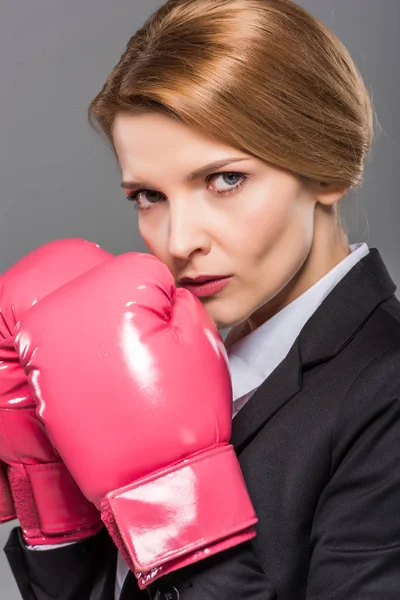 Femme d'affaires sérieuse en costume et gants de boxe rose, isolé sur gris — Photo de stock