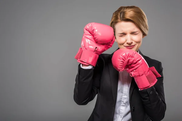 Stressed businesswoman in suit and pink boxing gloves, isolated on grey — Stock Photo