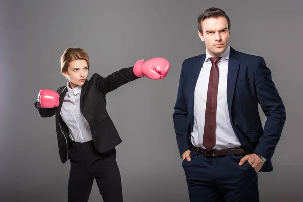 Confident businesswoman in boxing gloves and handsome businessman, isolated on grey, feminism concept — Stock Photo