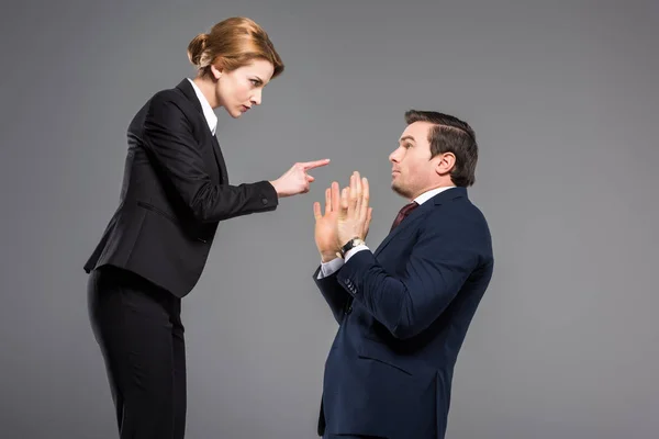 Donna d'affari arrabbiata litigando e indicando uomo d'affari spaventato, isolato su grigio — Foto stock