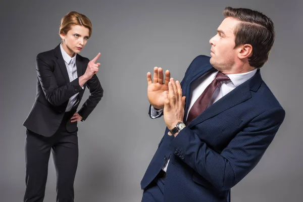 Aggressiva donna d'affari litigando e indicando uomo d'affari spaventato, isolato su grigio — Foto stock