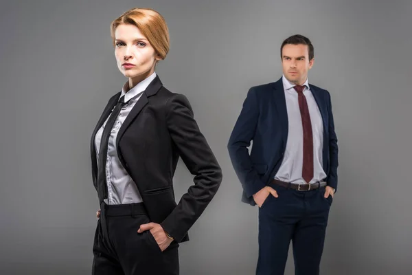 Confident businesswoman with hands in pockets and businessman standing behind, isolated on grey, feminism concept — Stock Photo