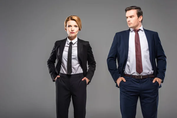 Seriöse Geschäftsfrau und Geschäftsmann posiert mit den Händen in den Taschen, isoliert auf grau — Stockfoto