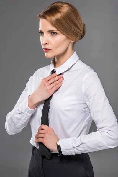 Empresaria confiada vistiendo corbata negra, aislada en gris - foto de stock