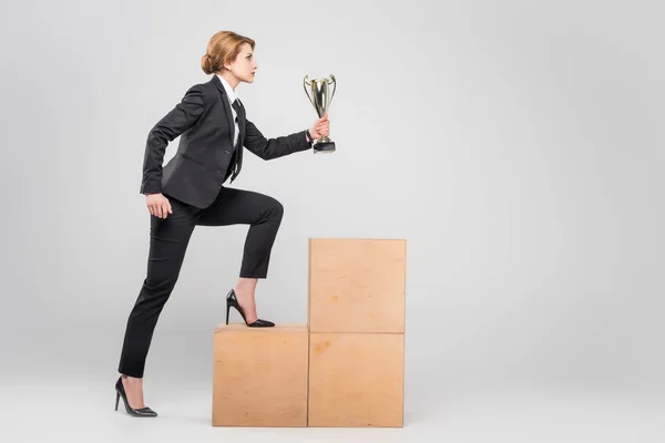 Empresaria con copa de trofeo subiendo al podio, aislada en gris — Stock Photo