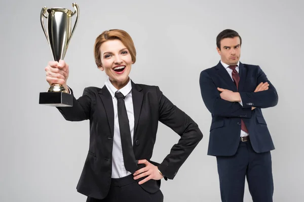 Excited businesswoman with award and upset businessman behind, isolated on grey — Stock Photo