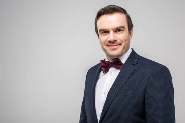 Happy groom in tuxedo and bow tie, isolated on grey — Stock Photo