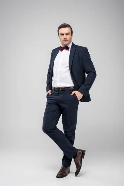 Handsome man posing in tuxedo with hands in pockets, isolated on grey — Stock Photo