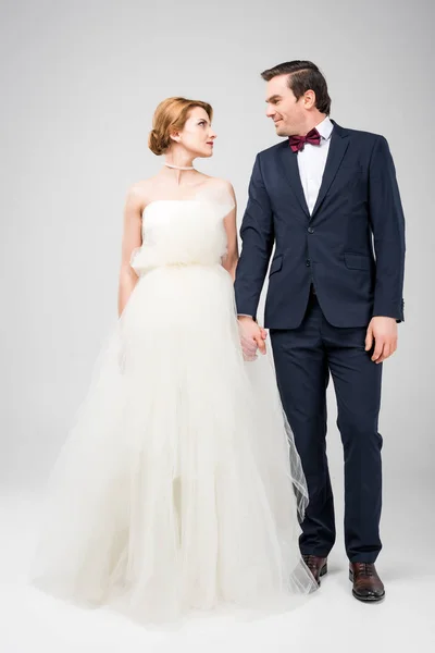 Наречений в смокінг і наречена у весільній сукні тримає руки, ізольовані на сірому — стокове фото