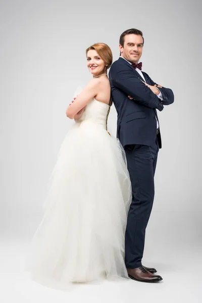 Pareja de boda de pie espalda con los brazos cruzados, aislado en gris - foto de stock