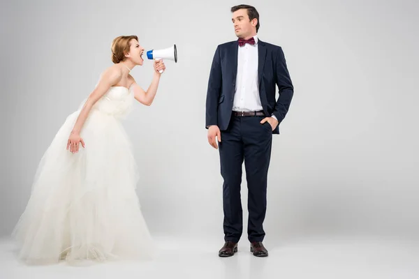 Angry bride with megaphone yelling at groom, isolated on grey, feminism concept — Stock Photo