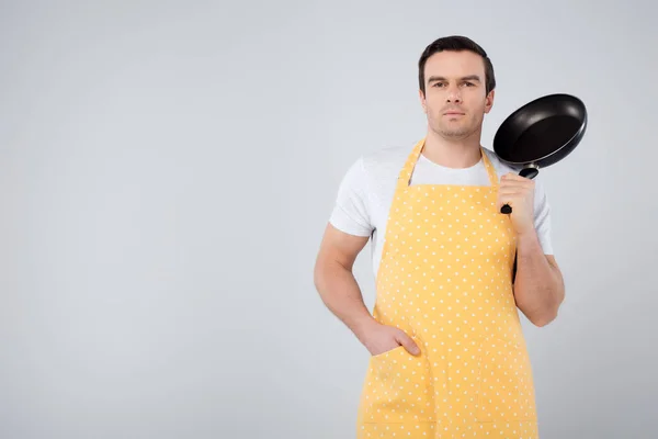 Männliche Haushälterin in gelber Schürze mit Bratpfanne, isoliert auf grau — Stockfoto