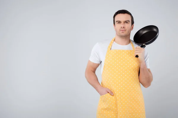 Male householder in yellow apron holding frying pan, isolated on grey — Stock Photo