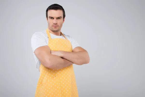 Chefe de família masculino em avental amarelo em pé com braços cruzados, isolado em cinza — Fotografia de Stock