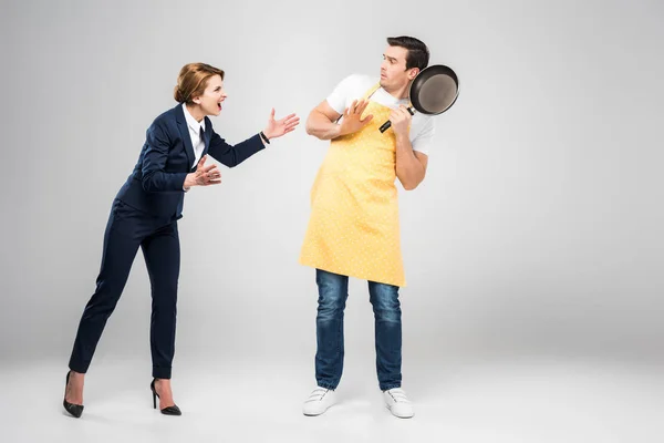 Businesswoman yelling at scared husband with frying pan, feminism concept, isolated on grey — Stock Photo