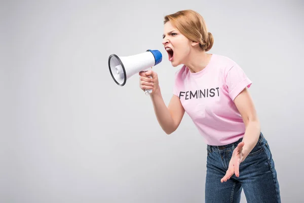 Donna in t-shirt rosa femminista che urla contro il megafono, isolata sul grigio — Foto stock