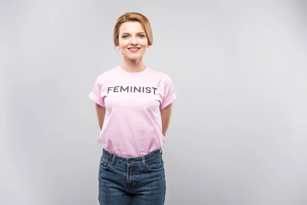 Donna sorridente in t-shirt femminista rosa, isolata sul grigio — Foto stock