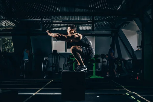 sportsman doing squats on cube