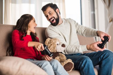 mutlu baba ve kızı evde video oyun oynarken ve birbirine bakarak