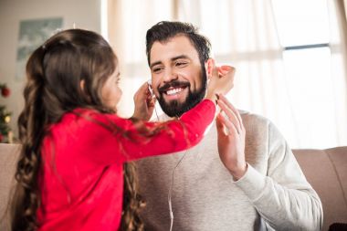 daughter plugging earphones into father ears clipart