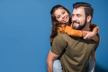 father giving piggyback to smiling daughter on blue clipart