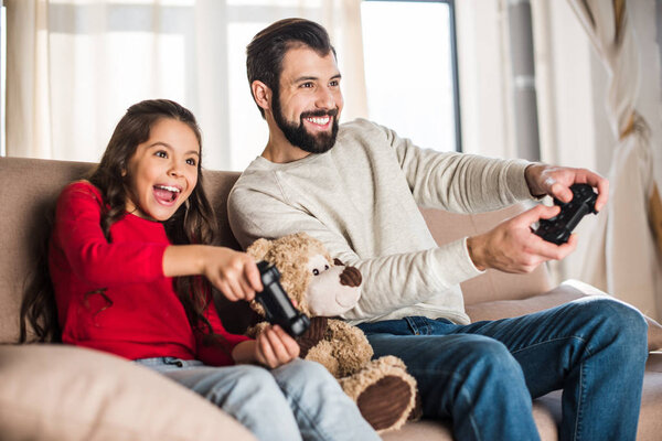 smiling father and daughter playing video game at home 