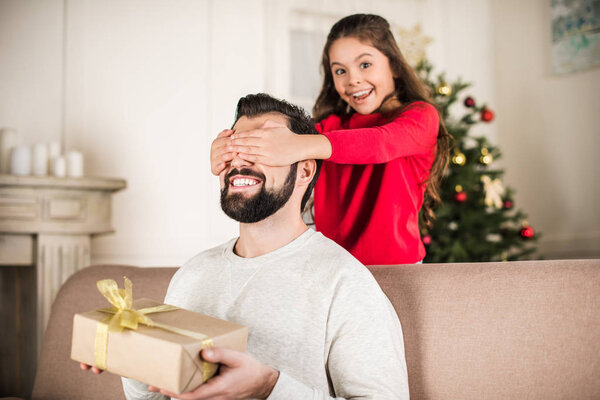 Улыбающаяся дочь, прикрывающая глаза отца
