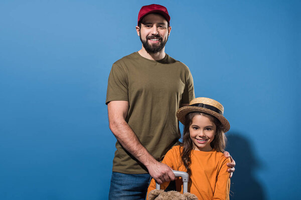father in cap and daughter in straw hat looking at camera on blue