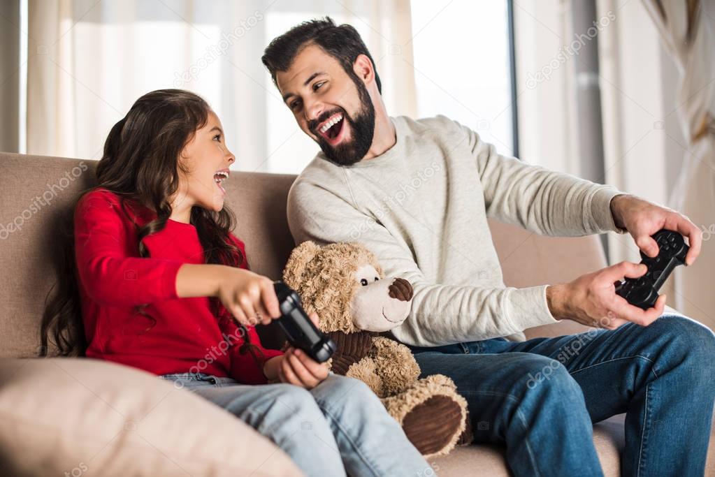 happy father and daughter playing video game at home and looking at each other