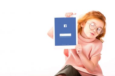 Kızıl saçlı çocuk oturan ve üzerinde beyaz izole tablet yüklü facebook sayfası gösterilen