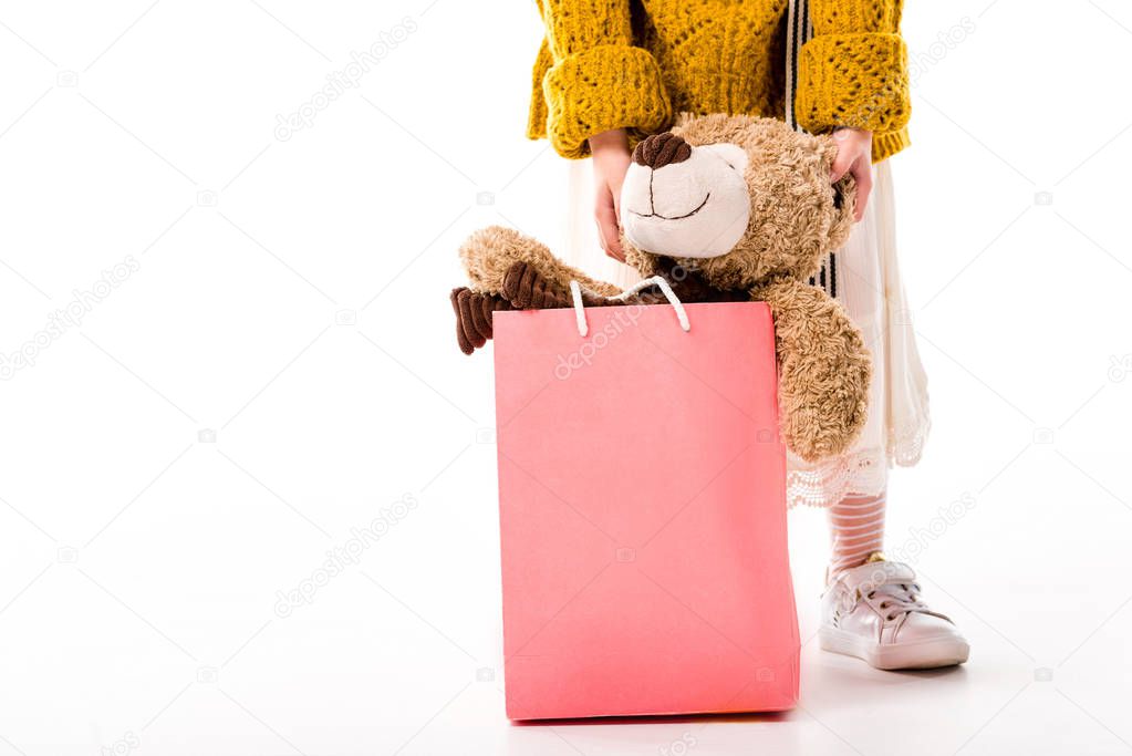 cropped image of kid standing with teddy bear in shopping bag on white