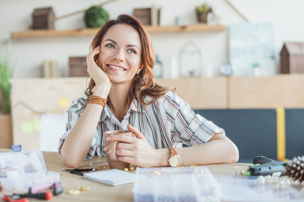 dreamy young woman with cup of coffee in handmade workshop