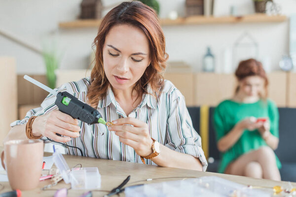 young woman using glue gun in handmade accessories workshop