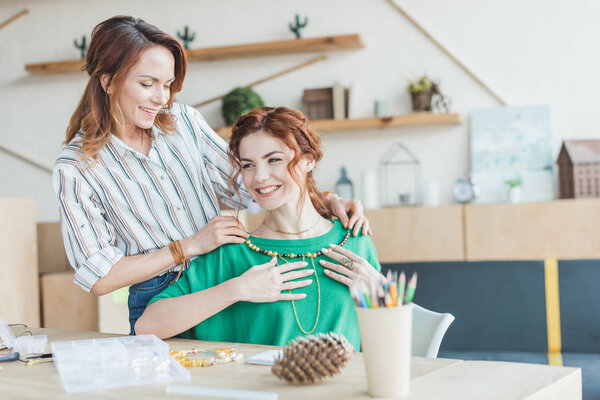 smiling young women trying on handmade necklace at workshop