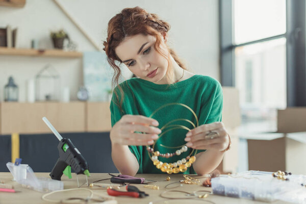 young woman holding handmade necklaces in workshop