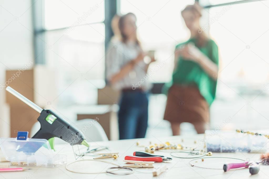 table with tools for handmade accessories manufactoring with blurred women drinking coffee on background