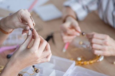 cropped shot of women making accessories of beads at workshop clipart