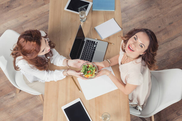 top view of coworkers holding bowl healthy salad at office