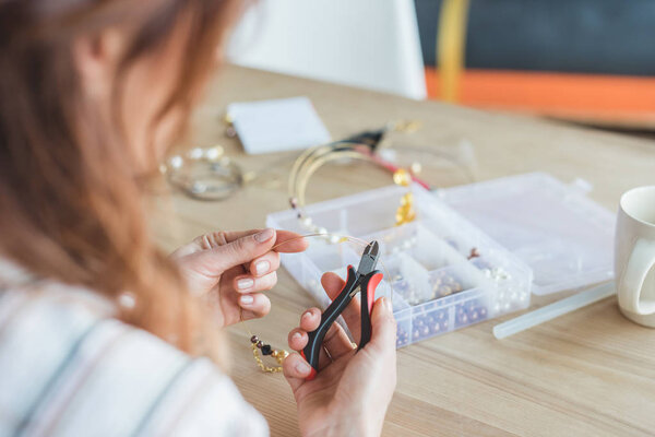 close-up shot of young woman making accessory with linesman pliers in workshop