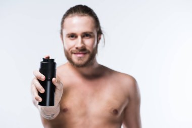 Deodorant sprey uzanmış elinde tutan neşeli genç adam 