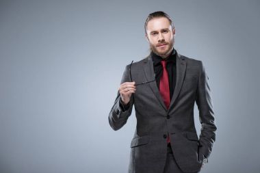 Gri izole kamera, el bakarak gözlüklü resmi elbiseli ciddi genç adam